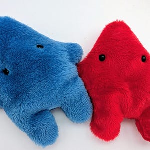 May include: Two plush toys shaped like five-pointed stars, one in bright blue and one in vibrant red. Each soft, fuzzy toy features two small black bead eyes positioned on the upper portion of the star shape, with two short limbs at the base.