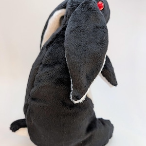 May include: A plush black and white rabbit toy with red eyes. The rabbit has long, floppy ears with white and tan accents. The soft toy is sitting upright, showcasing its fluffy texture.