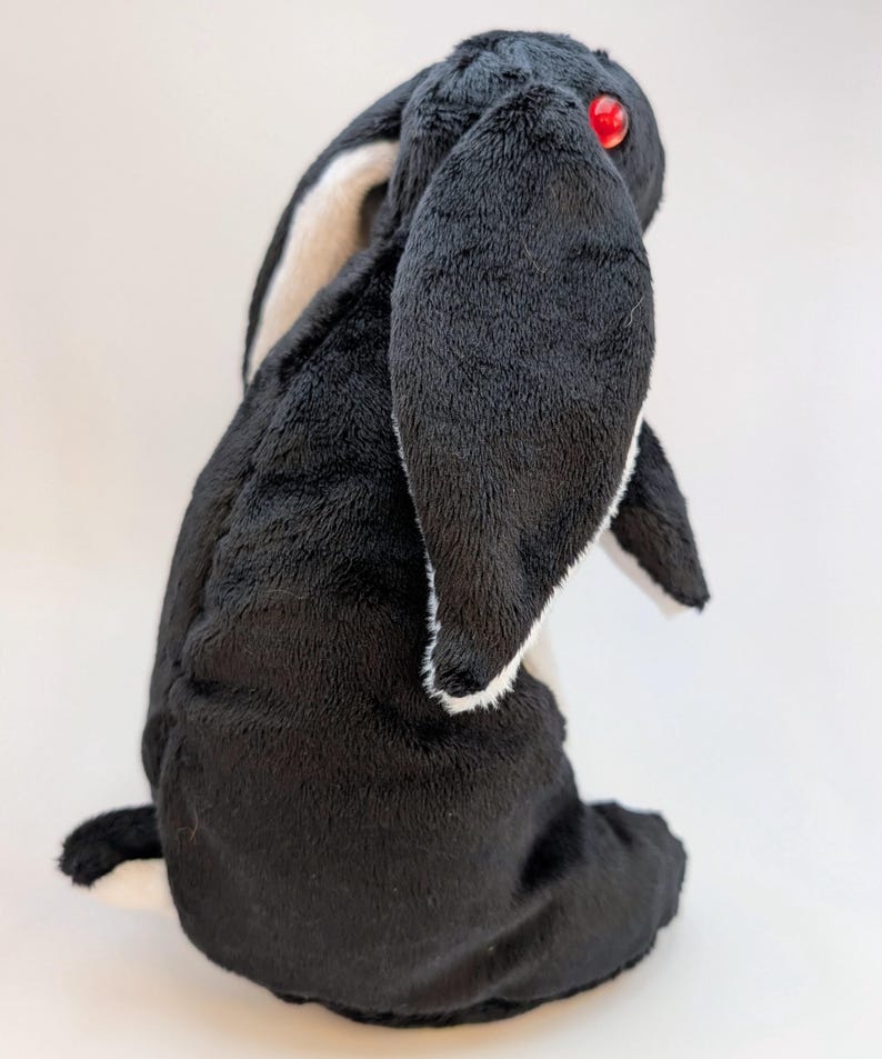 May include: A plush black and white rabbit toy with red eyes. The rabbit has long, floppy ears with white and tan accents. The soft toy is sitting upright, showcasing its fluffy texture.
