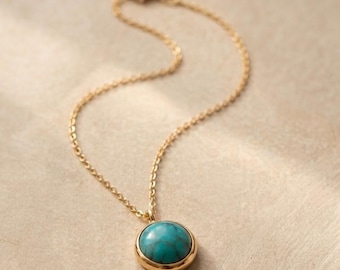 May include: A gold-toned necklace featuring a round pendant with a smooth, polished turquoise stone. The pendant is set in a simple gold-colored metal frame and hangs from a delicate, matching gold-toned chain with small, uniform oval links.