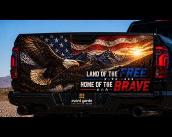 May include: A black pickup truck tailgate wrap featuring a bald eagle in flight over a mountain landscape with a sunset and an American flag. The text reads: LAND OF THE FREE HOME OF THE BRAVE. The design includes red, white, and blue color accents.