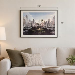 May include: A framed landscape art print featuring a surreal cityscape with tall buildings surrounding a deep chasm and a central island with palm trees. The artwork measures 24 inches in width by 18 inches in height, displayed in a thin black frame.
