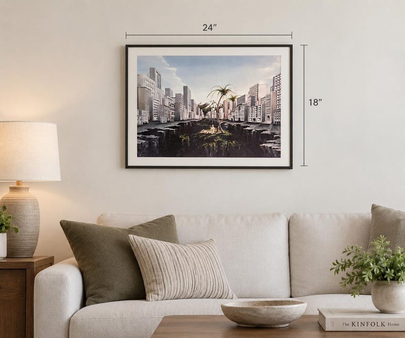 May include: A framed landscape art print featuring a surreal cityscape with tall buildings surrounding a deep chasm and a central island with palm trees. The artwork measures 24 inches in width by 18 inches in height, displayed in a thin black frame.