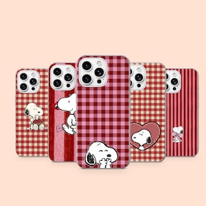 Puede incluir: Cinco fundas para smartphone con Snoopy en varias posturas. Los diseños incluyen patrones de cuadros vichy en rojo y rosa, rayas verticales rojas y un motivo de corazón. Cada funda muestra al personaje Snoopy con diferentes expresiones.