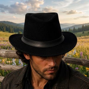 May include: A black felt fedora hat featuring a structured crown with a centre crease and a wide, slightly curved brim. The hat is accented with a smooth, black leather band encircling the base of the crown, providing a clean and uniform appearance.