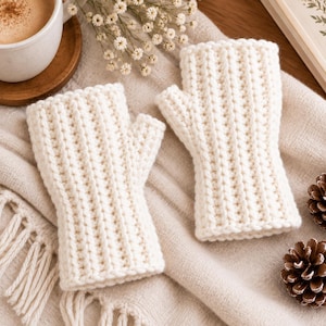 May include: A pair of off-white fingerless gloves featuring a vertical ribbed knit pattern. The gloves are designed with a thumb hole and cover the hand from the knuckles to the wrist, showcasing a thick, textured yarn construction throughout.
