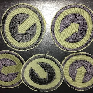 May include: Five circular patches with a green border and a black arrow design. The arrows point in different directions. The patches are on a dark surface.