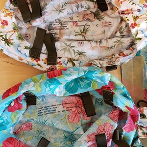 May include: Two fabric helmet covers with Hawaiian and Miami Marpat camouflage patterns. The covers are both medium/large size and have adjustable straps. The text on the covers reads: "COVER, HELMET, HAWAIIAN BODGA-LUAU CAMOUFLAGE DSA 100-20-F019 0786-01-103-2469 SABIA FABRICATORS, INC. MEDIUM LARGE" and "COVER HELMET, MIAMI MARPAT CAMOUFLAGE DSA 100-20-B-FU19 0786-01-103-2469 SABIA FABRICATOR CO., INC. EST. 2013 AD MEDIUM/"