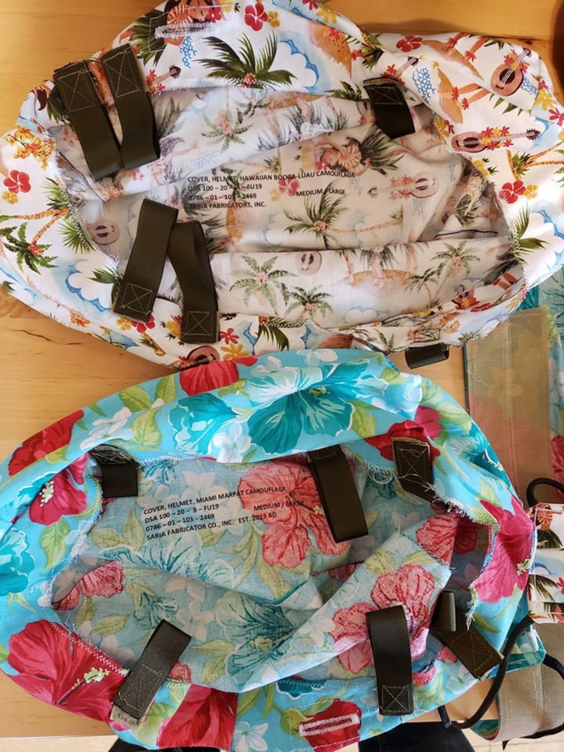 May include: Two fabric helmet covers with Hawaiian and Miami Marpat camouflage patterns. The covers are both medium/large size and have adjustable straps. The text on the covers reads: "COVER, HELMET, HAWAIIAN BODGA-LUAU CAMOUFLAGE DSA 100-20-F019 0786-01-103-2469 SABIA FABRICATORS, INC. MEDIUM LARGE" and "COVER HELMET, MIAMI MARPAT CAMOUFLAGE DSA 100-20-B-FU19 0786-01-103-2469 SABIA FABRICATOR CO., INC. EST. 2013 AD MEDIUM/"