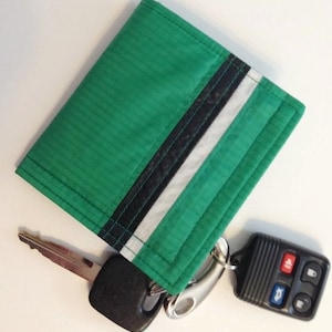 May include: A green wallet with black and white stripes and a silver key chain attached to a black car key.