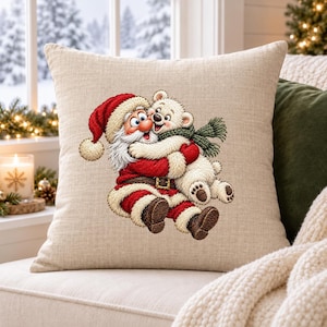 May include: A square beige throw pillow featuring a detailed embroidered illustration of Santa Claus wearing a red suit and hat, embracing a small white polar bear cub that is wearing a green knitted scarf around its neck.