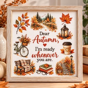 May include: A framed cross-stitch sampler featuring the text "Dear Autumn, I'm ready whenever you are." surrounded by seasonal motifs including a bicycle with flowers, a lantern, a coffee cup, a park bench with a blanket, books, and trees.