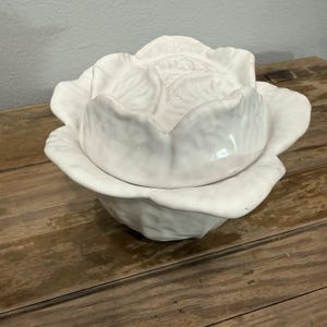 Op de afbeelding: Een witte keramische kom met deksel in de vorm van een kool. De kom heeft een gestructureerd, geplooid bladontwerp op zowel de basis als het afneembare deksel, wat zorgt voor een realistische groente-uitstraling met een gladde, glanzende afwerking.