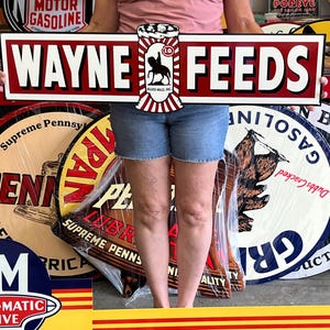 May include: A vintage "WAYNE FEEDS" sign with a red and white design, featuring the text "WAYNE FEEDS" in bold white letters on a red background. The sign includes a logo with a horse and the text "ALLIED MILLS INC.".
