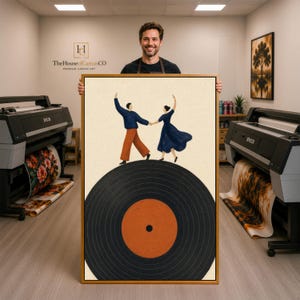May include: A rectangular framed wall art print featuring a stylized illustration of two figures dancing on a large black vinyl record with an orange center. The figures are holding hands, one wearing a blue sweater and orange pants, the other a blue dress.