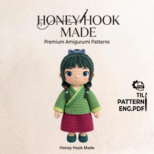 Könnte beinhalten: Eine gehäkelte Amigurumi-Puppe mit dunkelgrünem Haar, einer blauen Haarschleife und geflochtenen Zöpfen. Die Puppe trägt ein grünes Wickeloberteil mit gelbem Saum und einen dunkelrosa Rock. Text: HONEY HOOK MADE Premium Amigurumi Patterns und TIL PATTERN ENG.PDF.