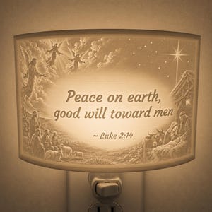 May include: A beige plug-in night light featuring a detailed nativity scene with angels, shepherds, sheep, and the holy family. The centre displays the text Peace on earth, good will toward men ~ Luke 2:14, illuminated by a warm, soft glow.