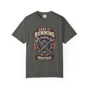 Pode incluir: Uma t-shirt cinzento-carvão de manga curta com uma impressão gráfica de uma engrenagem e chaves inglesas cruzadas. O texto KEEP IT RUNNING e INDUSTRIAL MAINTENANCE está em fonte clara, acentuado por símbolos de relâmpagos cor de laranja.