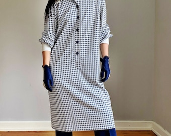 May include: A long-sleeved dress with a white collar and a blue and white houndstooth pattern. The dress has a button-up front and is worn with navy blue pants and red cowboy boots.