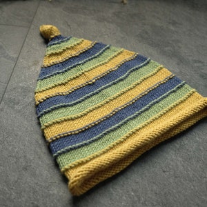 Peut inclure: Un bonnet en tricot rayé avec des rayures jaunes, vertes et bleues. Le bonnet a un sommet pointu et un bord plié.