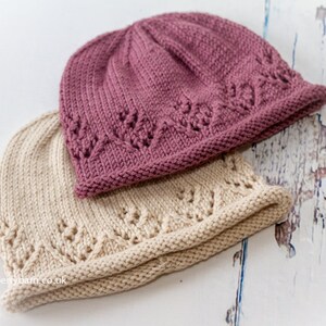 May include: Two knitted hats, one in a light beige color and the other in a dusty rose color. Both hats have a delicate stitch pattern and a folded brim.