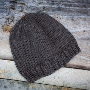 May include: A dark grey knitted beanie hat on a wooden surface.