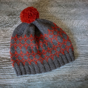 May include: A gray knitted beanie with a red pom pom and a geometric pattern.