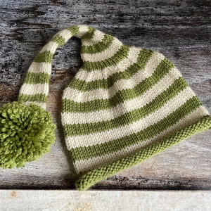 Puede incluir: Un gorro de punto de rayas verdes y blancas con una parte superior larga y puntiaguda y un pompón verde.