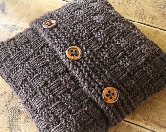 May include: A brown knitted cushion with three wooden buttons. The cushion is made with a woven stitch pattern.