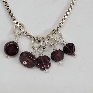 May include: A silver chain necklace with multiple dangling charms featuring dark red gemstone beads.