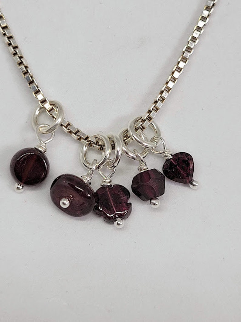 May include: A silver chain necklace with multiple dangling charms featuring dark red gemstone beads.