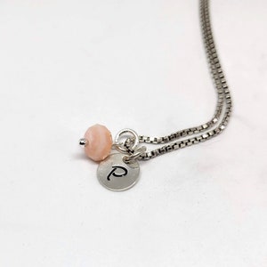 May include: A silver chain necklace with a pink bead and a silver charm with the letter "P" engraved on it.