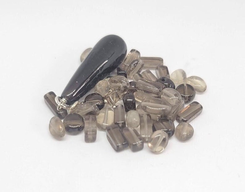 May include: A collection of smoky quartz beads in various shapes and sizes, including round, oval, and rectangular beads. A black teardrop-shaped pendant is included.