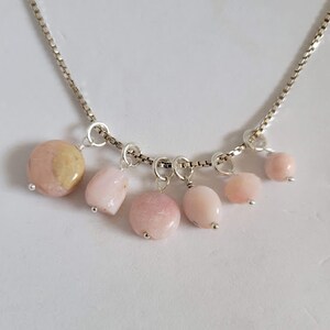 May include: A silver chain necklace with six pink and white opal stones hanging from it. The stones are various shapes and sizes.