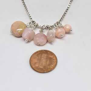 May include: A silver chain necklace with six pink and peach opal gemstone beads. The necklace is about the size of a US penny.