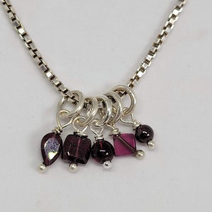 May include: A silver chain necklace with a cluster of small purple and clear glass beads hanging from it. The beads are attached to the chain with silver rings.