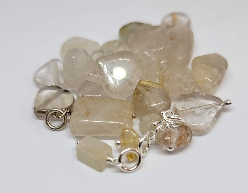 May include: A pile of clear quartz crystals with a silver chain and clasps. The crystals are various shapes and sizes.