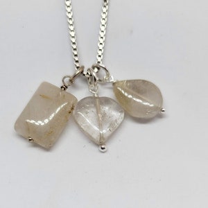 May include: A silver chain necklace with three clear quartz crystal pendants: a rectangle, a heart, and a teardrop.