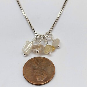 May include: A silver chain necklace with five small, dangling charms. The charms are made of clear, white, and yellow stones.