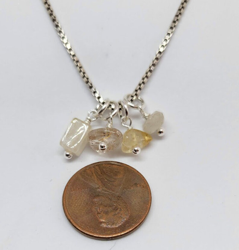 May include: A silver chain necklace with five small, dangling charms. The charms are made of clear, white, and yellow stones.