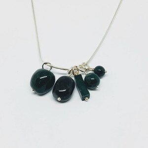 May include: A silver chain necklace with multiple dark green gemstone charms. The charms include round beads, oval stones, and a rectangular stone.