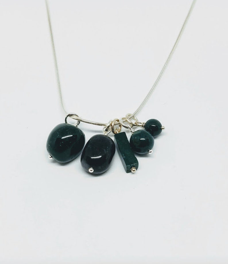 May include: A silver chain necklace with multiple dark green gemstone charms. The charms include round beads, oval stones, and a rectangular stone.