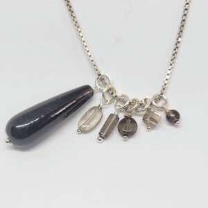May include: A silver chain necklace with a black teardrop-shaped pendant and multiple smaller gray and brown gemstone charms.