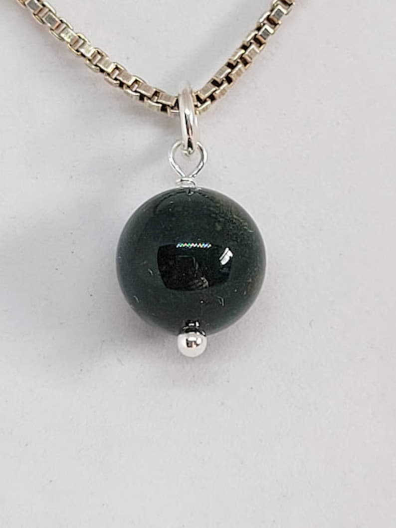 May include: A silver chain necklace with a dark green gemstone pendant. The pendant is a round ball with a smooth, polished surface.