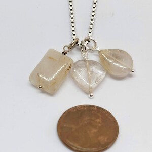 May include: A silver chain necklace with three clear quartz crystal pendants. The pendants are a rectangle, a heart, and a teardrop shape.