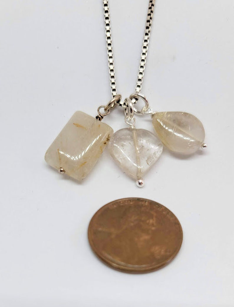 May include: A silver chain necklace with three clear quartz crystal pendants. The pendants are a rectangle, a heart, and a teardrop shape.
