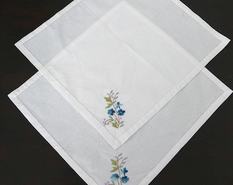 May include: Two white linen napkins with embroidered blue flowers and green leaves.