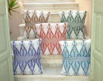 Puede incluir: Cinco cojines decorativos con patrones geométricos en tonos marrón, verde, rojo, azul y turquesa. Los cojines están dispuestos en un conjunto de escaleras blancas.