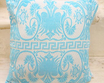 Puede incluir: Una almohada blanca con un patrón floral azul. El patrón presenta flores y hojas estilizadas, con un borde repetido de una llave griega.