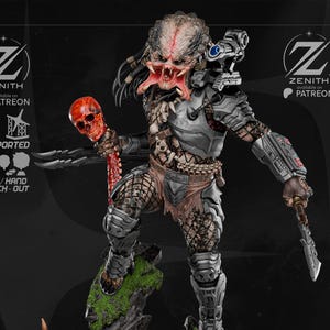 May include: A detailed Predator figurine standing on a rocky base adorned with multiple human skulls and moss. The creature wears metallic armor, carries a red skull trophy, and features a shoulder-mounted cannon. The base displays the text PREDATOR.